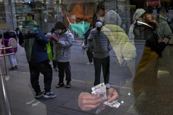 Visitors are reflected on a window pane as a man counts Chinese currency notes at a shop selling tea in Qianmen, a popular tourist spot in Beijing, Tuesday, Jan. 3, 2023. As the virus continues to rip through China, global organizations and governments have called on the country start sharing data while others have criticized its current numbers as meaningless. (AP Photo/Andy Wong)