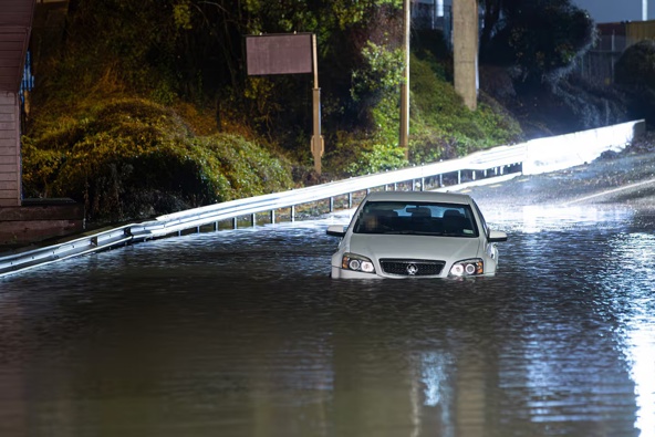 A man climbed out of his car window after becoming trapped by floodwaters on Onehunga Harbour Road, Onehunga, early on Saturday morning. Photo / Hayden Woodward