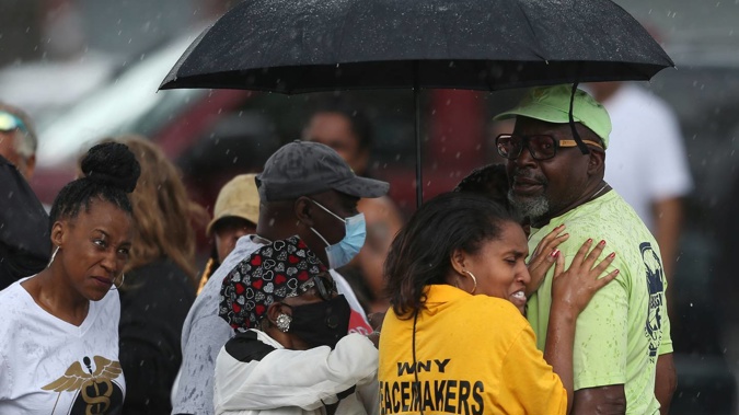 Bystanders gather under an umbrella as rain rolls in after a shooting at a supermarket in Buffalo, New York. (Photo / AP)