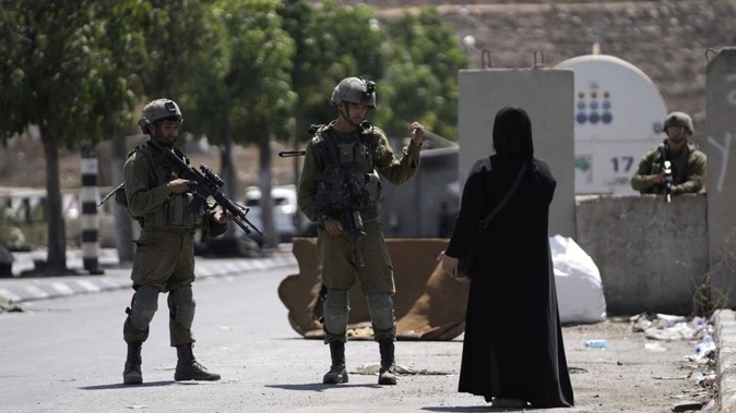 Israeli soldiers speak to a Palestinian woman near the site of an alleged car-ramming attack near Beit Hagai, a Jewish settlement in the hills south of the large Palestinian city of Hebron. Photo / AP