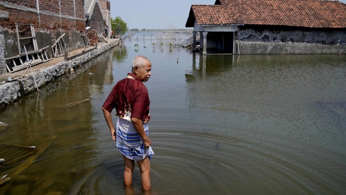 Sukarman walks on a flooded pathway outside his house in Timbulsloko, Central Java, Indonesia, in July last year. Photo / File