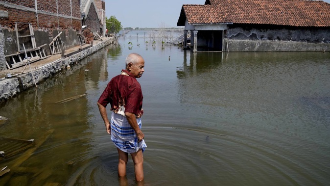 Sukarman walks on a flooded pathway outside his house in Timbulsloko, Central Java, Indonesia, in July last year. Photo / File