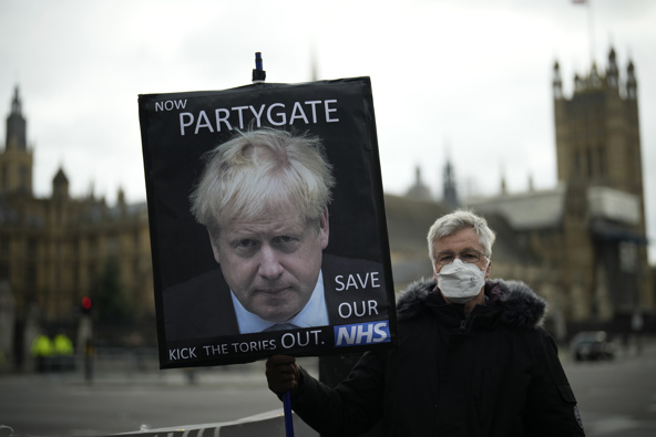An anti-Conservative Party protester holds a placard with an image of British Prime Minister Boris Johnson including the words "Now Partygate" backdropped by the Houses of Parliament, in London. (Photo / AP)