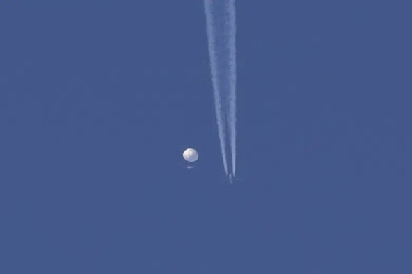 In this photo provided by Brian Branch, a large balloon drifts above the Kingstown, N.C. area, with an airplane and its contrail seen below it. The United States says it is a Chinese spy balloon moving east over America at an altitude of about 60,000 feet (18,600 meters), but China insists the balloon is just an errant civilian airshipused mainly for meteorological research that went off course due to winds and has only limited “self-steering” capabilities. (Brian Branch via AP)