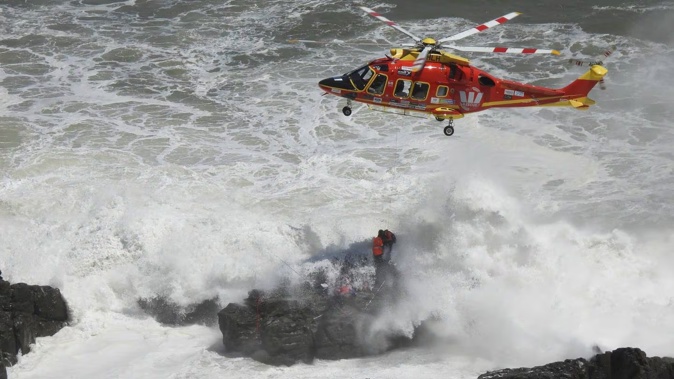 Two fishermen are winched to safety by the Auckland Westpac Rescue Helicopter from rocks at Sunset Beach, Port Waikato, as large swells threaten to wash the pair into the ocean. Photo / Auckland Rescue Helicopter Trust 
