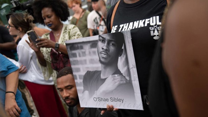 A person holds up a photo of O'Shae Sibley during a vigil. Photo / AP
