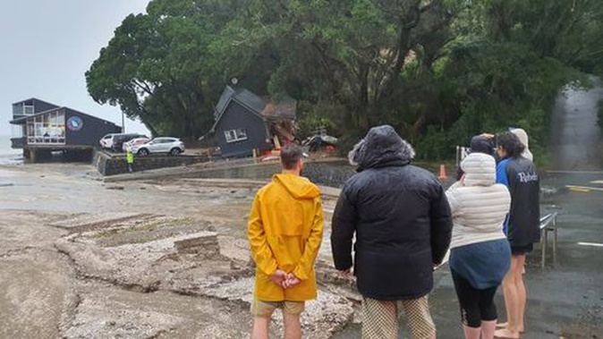 Residents at French Bay in Auckland watch on after a slip damaged the Coastguard building. Photo / Meg Liptrot