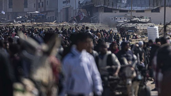 An Israeli army tank takes up position as Palestinians arrive in the southern Gaza town of Rafah after fleeing an Israeli ground and air offensive in the nearby city of Khan Younis. Israel has expanded its offensive in Khan Younis, saying the city is a stronghold of the Hamas militant group. Photo / AP