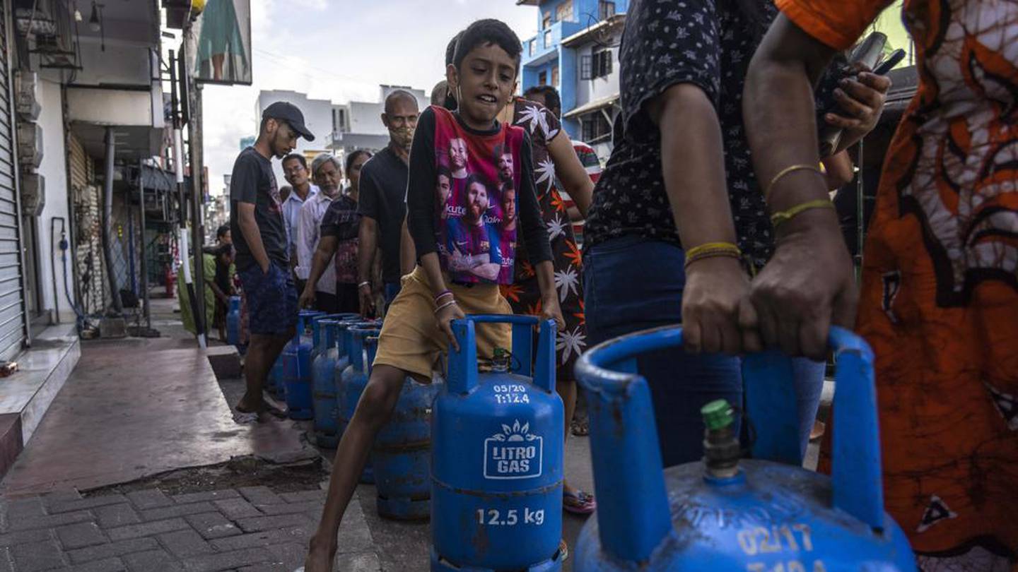 A boy tries to lift an empty cylinder as he along with others wait in a queue to buy domestic gas at a distribution center, in Colombo, Sri Lanka. Photo / AP