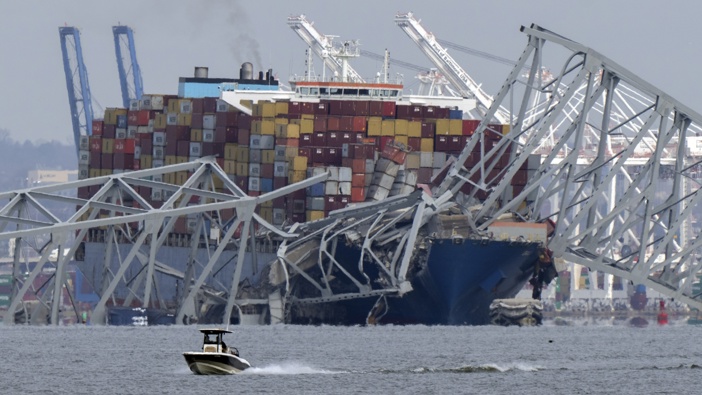 A boat moves past a container ship as it rests against wreckage of the Francis Scott Key Bridge. Photo / AP