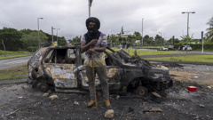 A man stands in front a burnt car after unrest in Noumea, New Caledonia, Wednesday May 15, 2024. France has imposed a state of emergency in the French Pacific territory of New Caledonia. The measures imposed on Wednesday for at least 12 days boost security forces' powers to quell deadly unrest that has left four people dead, erupting after protests over voting reforms. (AP Photo/Nicolas Job)