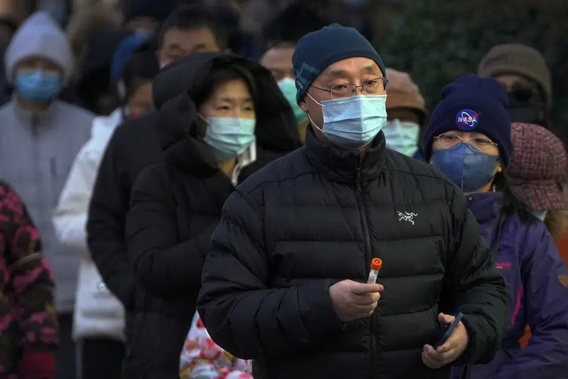 A man wearing a face mask holds his testing tube as masked residents line up for their routine COVID-19 throat swabs at a coronavirus testing site in Beijing, Sunday, Dec. 4, 2022. China on Sunday reported two additional deaths from COVID-19 as some cities move cautiously to ease anti-pandemic restrictions amid increasingly vocal public frustration over the measures. (AP Photo/Andy Wong)