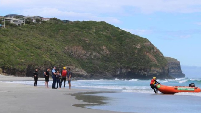 Police talk to a youth who managed to get back to shore after being swept out to sea on a bodyboard by a rip at Tomahawk Beach, Dunedin, while surf rescue stand by. Photo / Oscar Francis