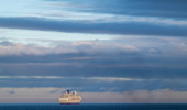 Cruise ship peacefully sailing on a calm ocean under a vast, cloud-filled sky - stock photo