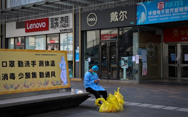 A man wearing a face mask browses his smartphone as he takes a rest on a bench displaying a coronavirus prevention poster near shuttered shops in Huaqiangbei, the world's biggest electronics market, in Shenzhen on March 14, 2022. (Photo / AP) 
