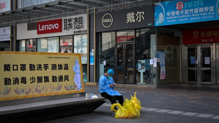 A man wearing a face mask browses his smartphone as he takes a rest on a bench displaying a coronavirus prevention poster near shuttered shops in Huaqiangbei, the world's biggest electronics market, in Shenzhen on March 14, 2022. (Photo / AP)
