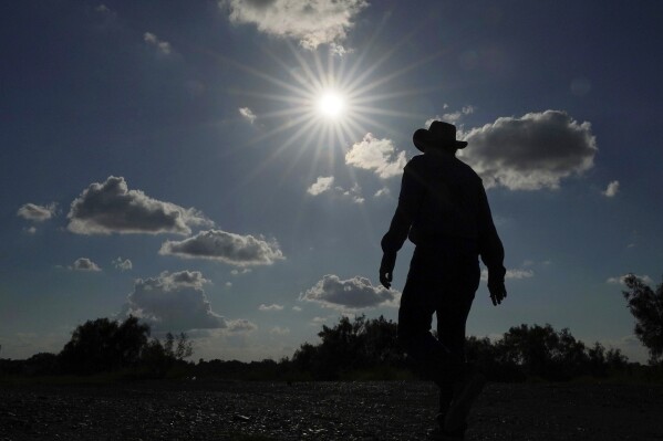 Kayak and canoe outfitter Jessie Fuentes walks along the Rio Grande under a warm sun Thursday, July 6, 2023. As the heat breaks records, weakening and sickening people, it’s worth remembering that dire heat waves have inspired effective efforts to prevent heat illness. (AP Photo/Eric Gay, File)