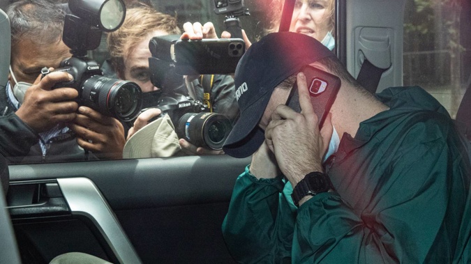 An unidentified man hides his face as members of the media photograph a car departing the offices of Serbian tennis player Novak Djokovic's legal team. Photo / Getty Images.