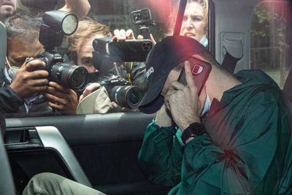 An unidentified man hides his face as members of the media photograph a car departing the offices of Serbian tennis player Novak Djokovic's legal team. Photo / Getty Images.