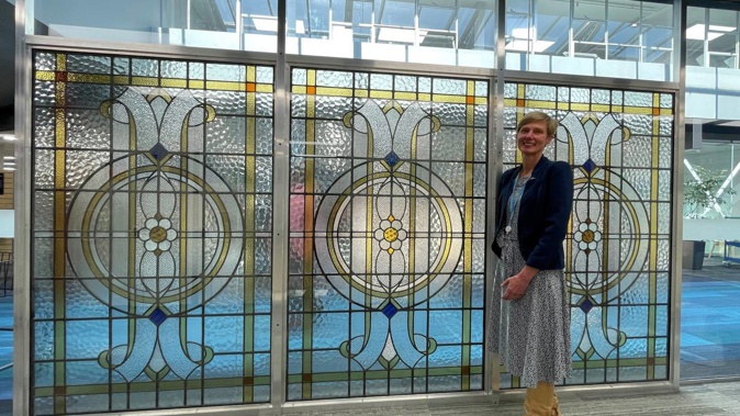 Libraries Manager Joanna Thomas standing in front of glass panels originally from the 1930s art deco building that housed the public library and electricity department. Photo / Supplied