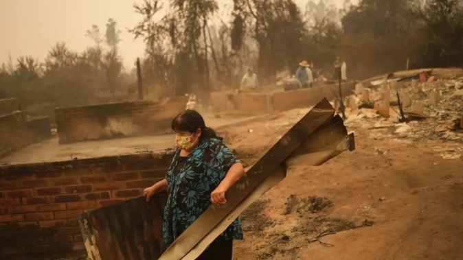 A woman clears debris from a landscape of charred remains in Santa Ana, Chile. Photo / AP
