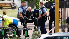 Wheelchair user Sean Nicholas is carried by police out of Albert Park in Auckland Central after an hours-long standoff in which he claimed to have "enough explosive material to level the Sky Tower". Photo / Dean Purcell