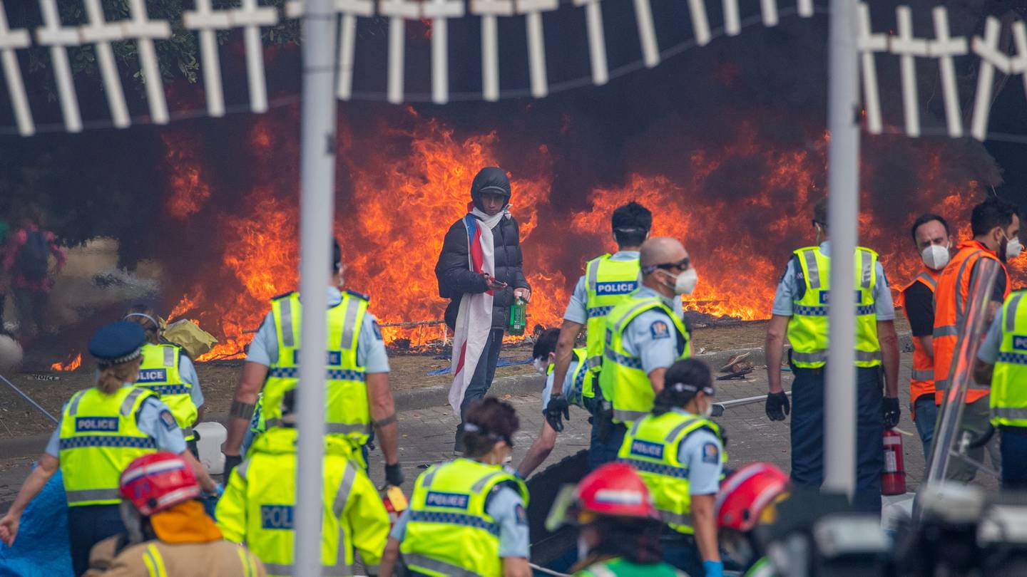 A lone protester facing Police officers in front of burning tents on day 23 of the Covid-19 Convoy. Photo / Mark Mitchell