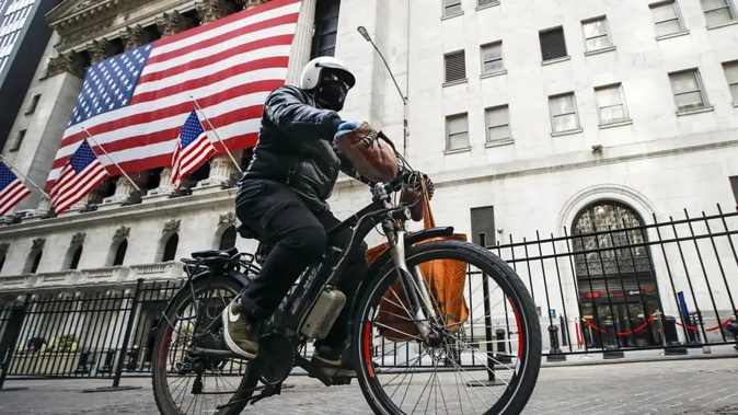 A delivery worker rides his electric bicycle past the New York Stock Exchange. Photo / AP