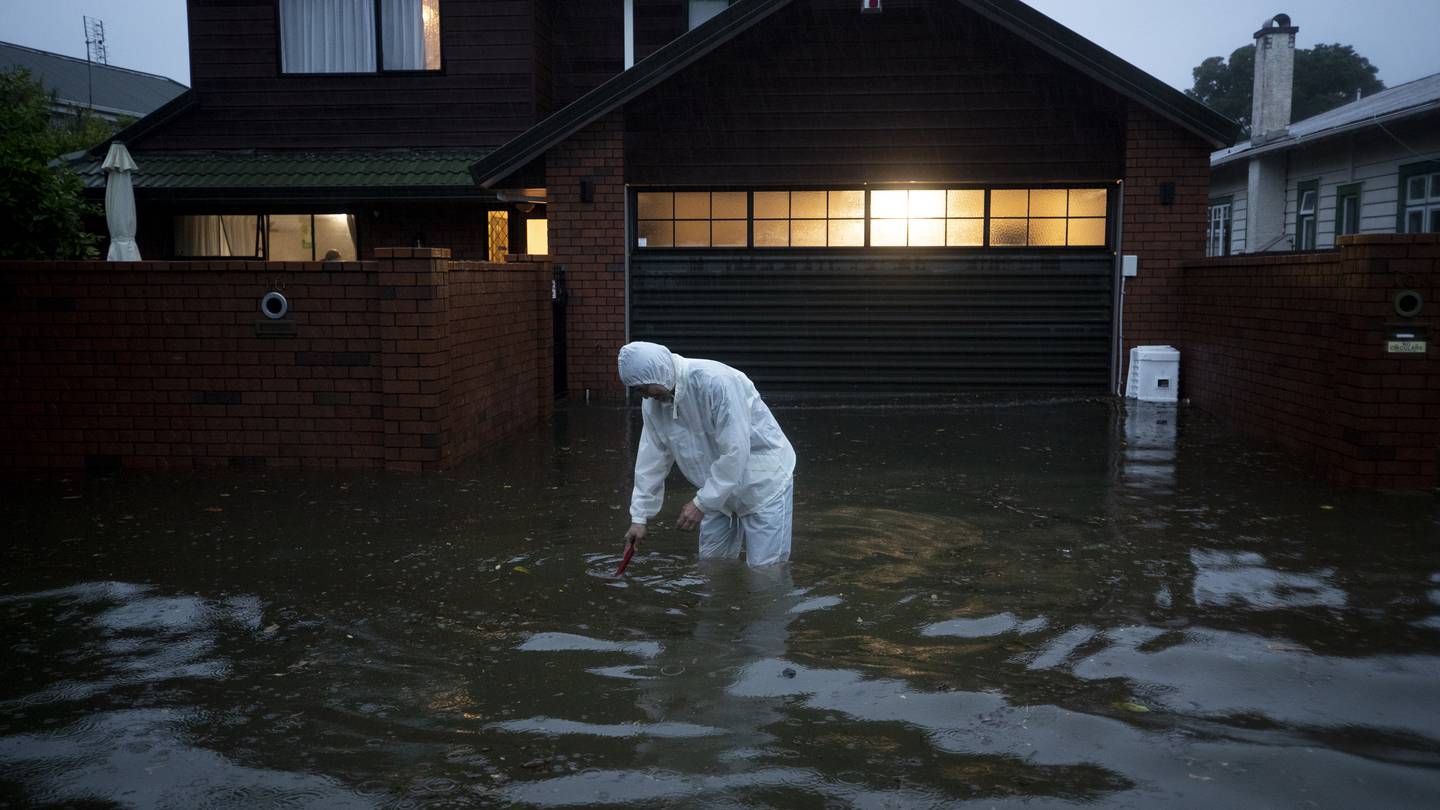 A man tries to clear the drain outside his house in Greenlane during the worst flooding the Auckland region has ever experienced. Photo / Dean Purcell