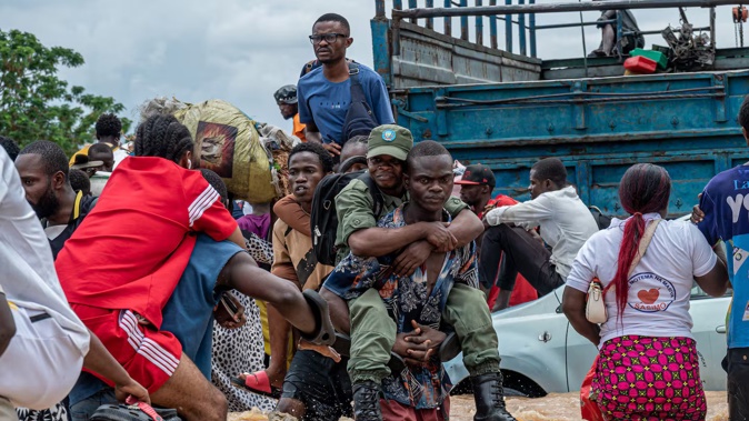 A resident carries a Congolese soldier as others wade through floodwaters in the Ndjili district of Kinshasa. Photo / AFP
