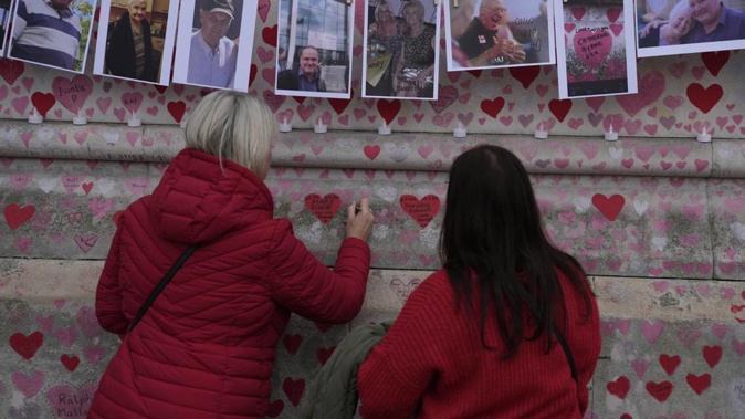 Family members write a message to two sisters who died of Covid on the National Covid Memorial wall in London in March. Photo / AP