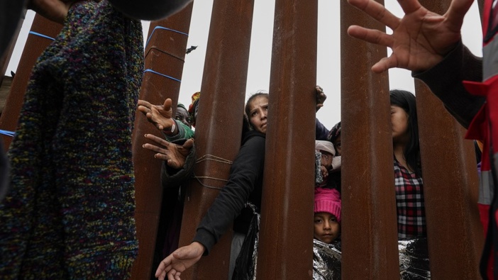 Migrants reach through a border wall for clothing handed out by volunteers as they wait between two border walls to apply for asylum on May 12, 2023, in San Diego. Photo / AP