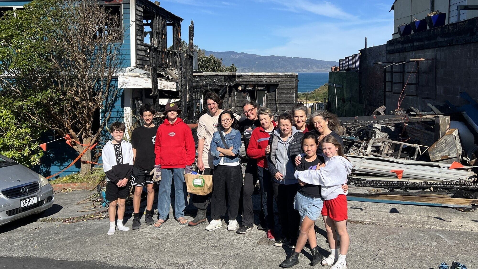 Schamet Horsfield (sixth from left) says her neighbours (pictured) surrounded her with love and support after the fire that burned down her dream home in Wellington's Island Bay.