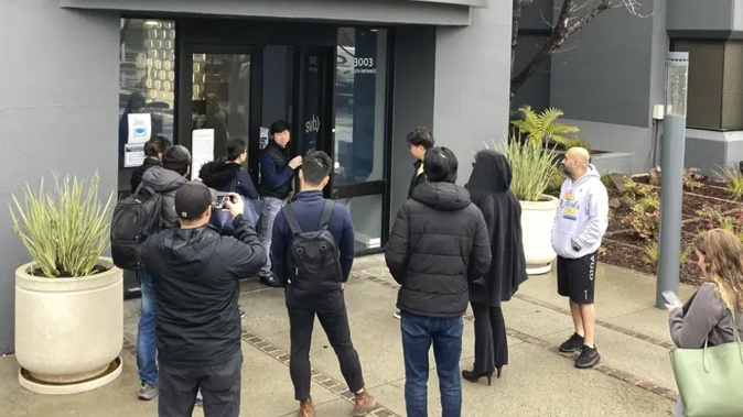 A person from inside Silicon Valley Bank, middle rear, talks to people waiting outside the headquarters of Silicon Valley Bank. Photo / AP