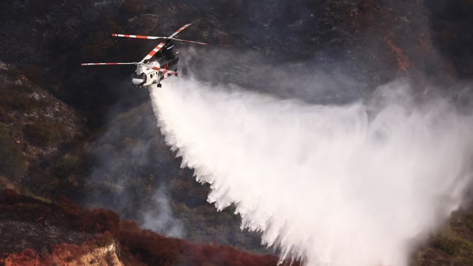 A firefighting helicopter drops water on a mountainside as the Franklin Fire burns in Malibu, California. Photo / AFP