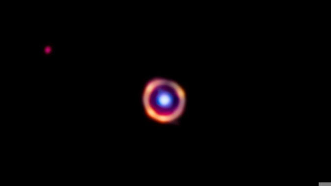 Astronomers using the Webb telescope discovered complex organic molecules in a galaxy located over 12 billion light-years away. The galaxy aligns almost perfectly with a second galaxy 3 billion light-years away from Earth. Webb captured the foreground galaxy in blue, while the more distant background galaxy is in red. The molecules appear in orange. J. Spilker/S. Doyle/NASA/ESA/CSA