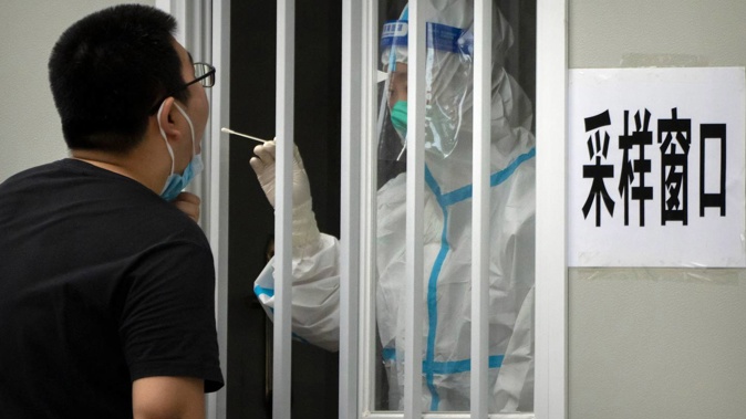 A worker wearing a protective suit swabs a man's throat for a Covid-19 test at a coronavirus testing site in Beijing. Photo / AP
