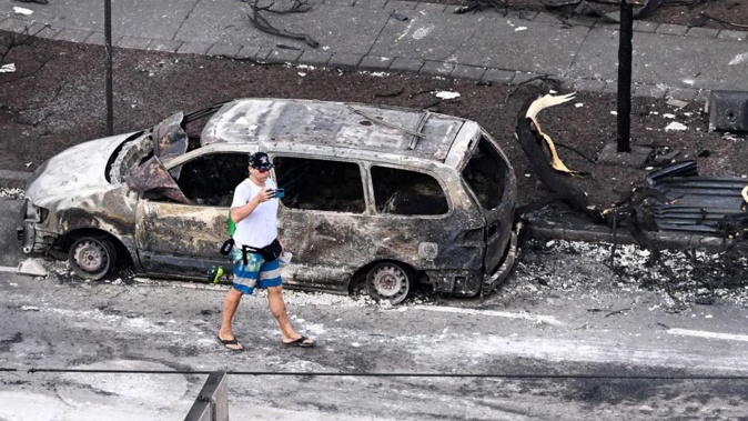 A tourist roams through burned cars on the streets of Lahaiana, Hawaii, following Maui fires. Photo / Getty Images