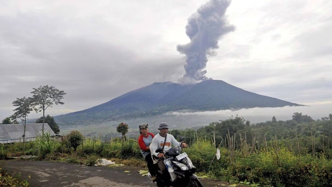 Motorists ride past by as Mt Marapi spews volcanic materials during its eruption in Agam, West Sumatra, Indonesia. Photo / AP