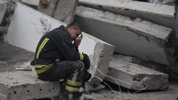 A rescue worker takes a pause as he sits on the debris at the scene where a woman was found dead after a Russian attack that heavily damaged a school. Photo / AP