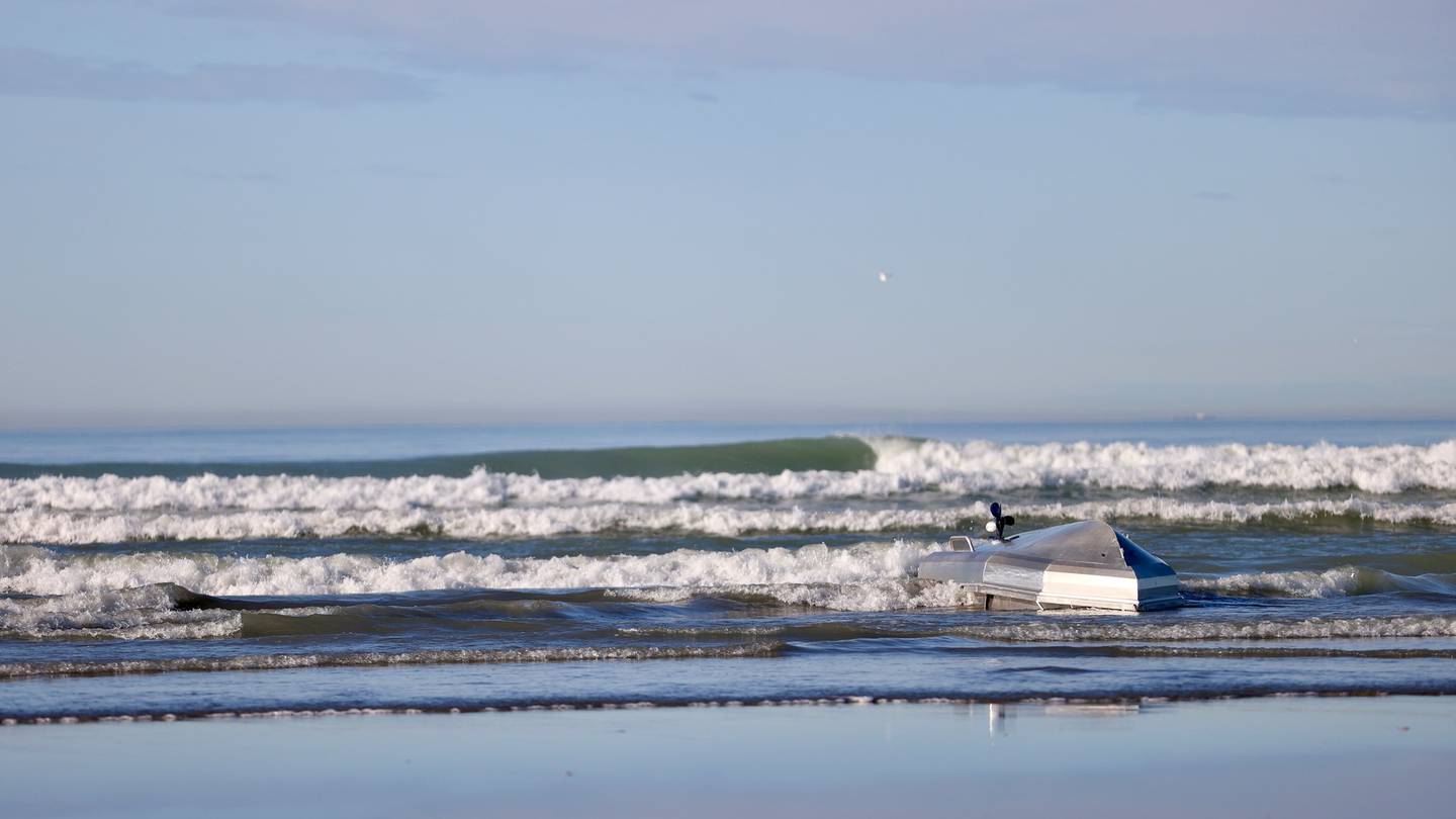 The overturned alumunium craft in the surf on Kairaki Beach after two boaties were rescued by nearby surfers. Photo / George Heard
