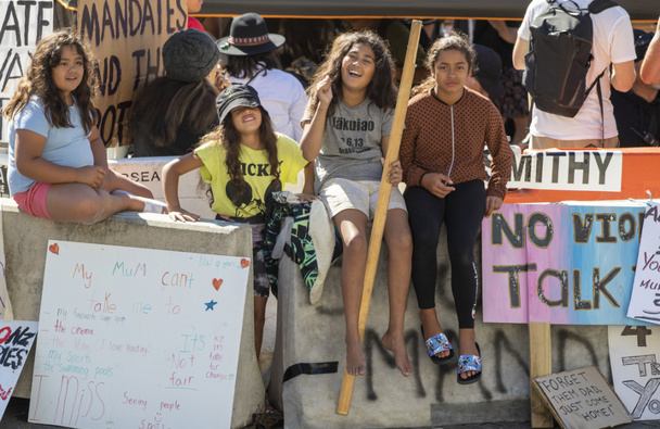 Children sitting on concrete barricades on the forecourt during day 14 of the Covid-19 convoy protest and occupation at Parliament, Wellington. 21 February, 2022. (Photo / Mark Mitchell)