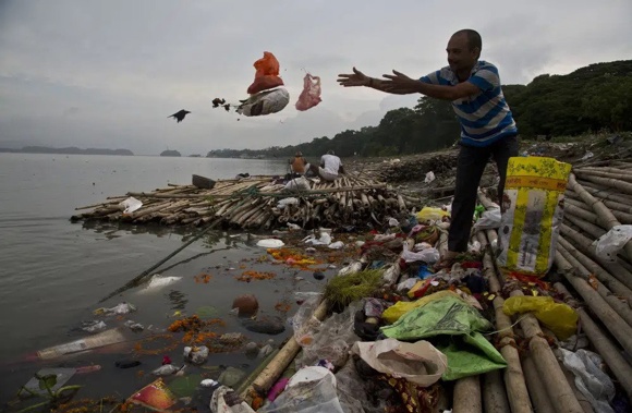 A Hindu devotee throws flowers and plastic bags into river Brahmaputra in Gauhati, India, Wednesday, Oct. 9, 2019. Negotiators from around the world gather at UNESCO in Paris on Monday, May 29, 2023, for a second round of talks aiming toward a global treaty on fighting plastic pollution in 2024. (AP Photo/Anupam Nath, File)