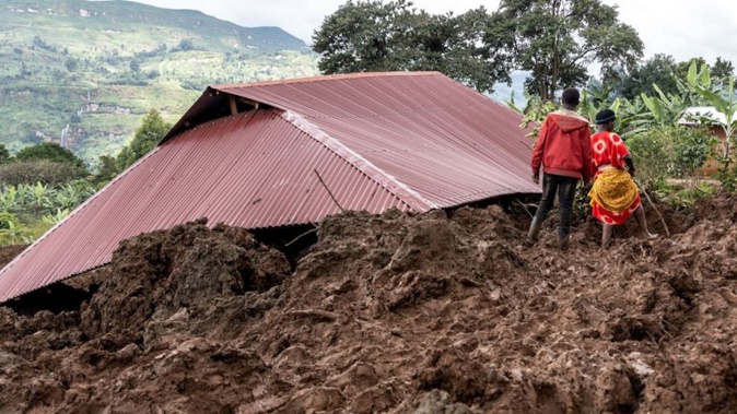 Residents walk past a house buried in mud after flooding and landslides in Masugu. Photo / AFP