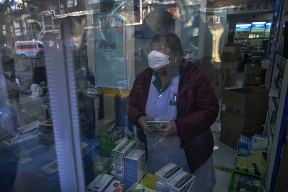 Residents are reflected on a door panel as they wait in line to buy medicine at a pharmacy in Beijing, Tuesday, Dec. 13, 2022. Some Chinese universities say they will allow students to finish the semester from home in hopes of reducing the potential of a bigger COVID-19 outbreak during the January Lunar New Year travel rush. (AP Photo/Andy Wong)