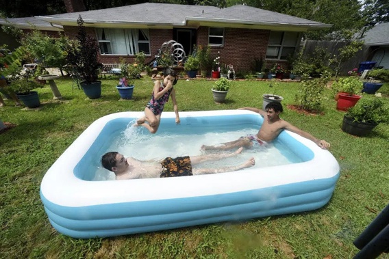 From left to right, Cason Bullis, Mya Kampfer and Caleb Dessos find a way to cool off with their inflatable pool, Saturday afternoon, June 17, 2023, in the front yard of their Shreveport, La., house that continues to be without electricity because of a storm on Friday evening, June 16. (Henrietta Wildsmith/The Shreveport Times via AP)