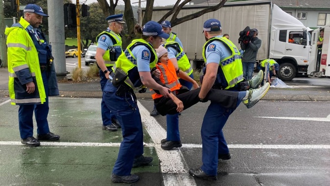 Restore Passenger Rail protester Jennifer Olsen is carried away by police after gluing herself to the road last week. Photo / Vita Molyneux