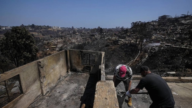 Residents clean up amid the rubble of homes burned by deadly forest fires in Vina Del Mar. Photo / AP