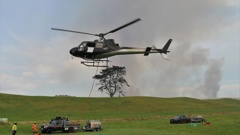 A helicopter equipped with a monsoon bucket takes off from the refuelling base set up on Srhoj Rd, Waiharara. Photo / Peter de Graaf
