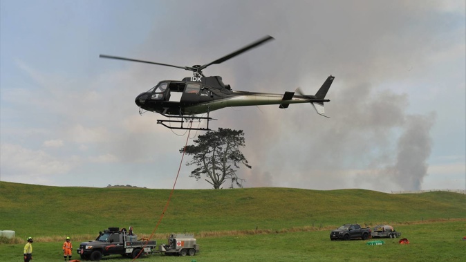 A helicopter equipped with a monsoon bucket takes off from the refuelling base set up on Srhoj Rd, Waiharara. Photo / Peter de Graaf